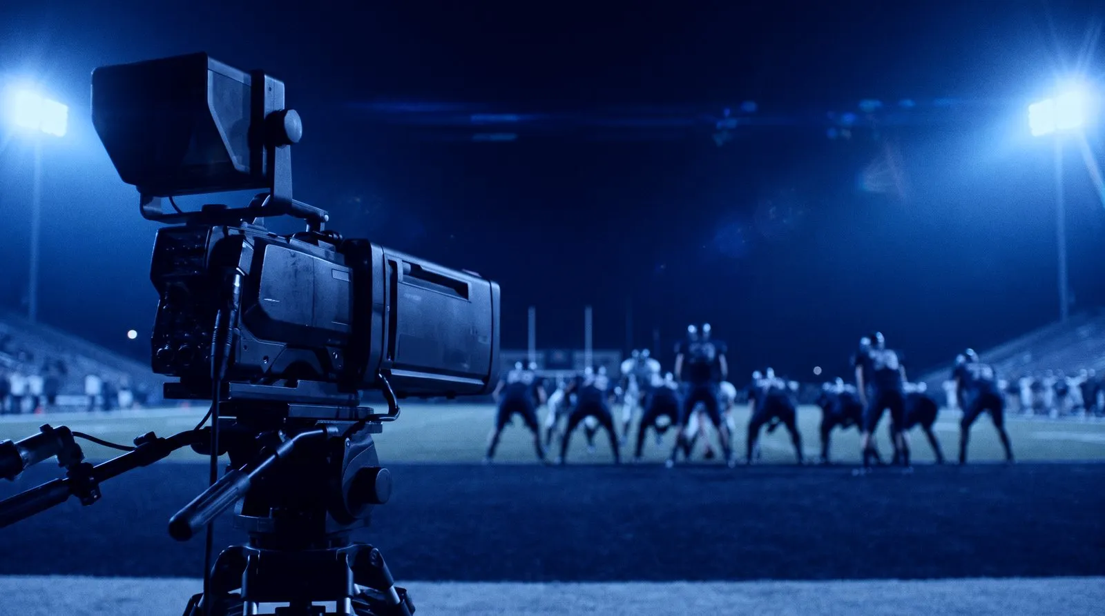 Broadcast cameras covering a football game under stadium lights